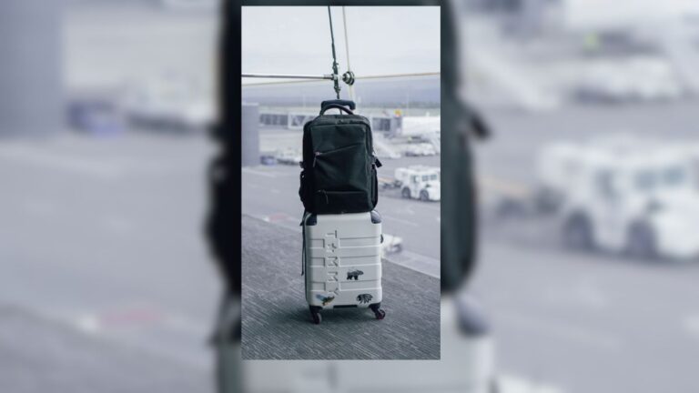 Personal item backpack resting on a carry-on suitcase at an airport