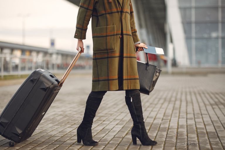 Traveler pulling a carry-on suitcase outside an airport terminal.