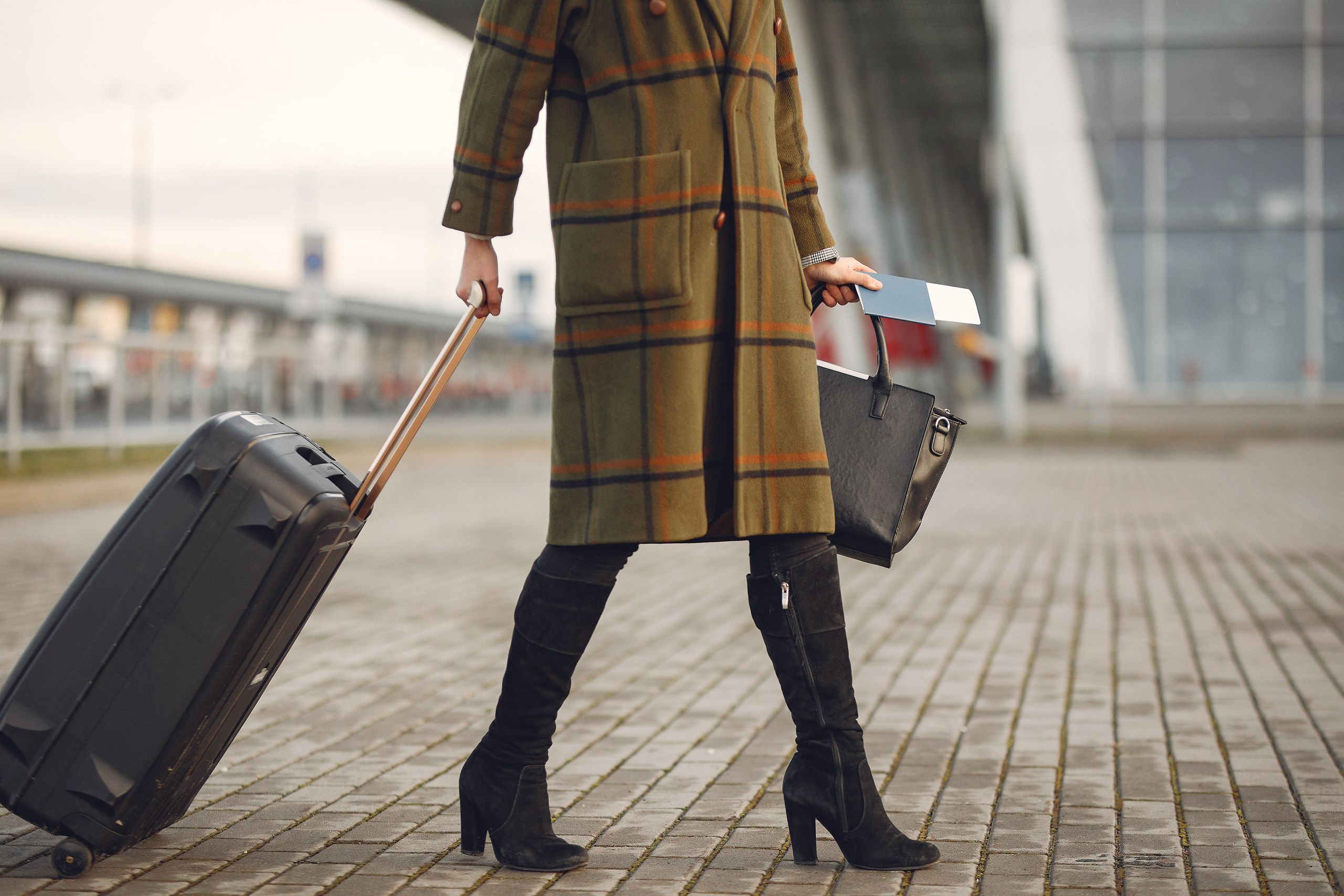 Traveler pulling a carry-on suitcase outside an airport terminal.