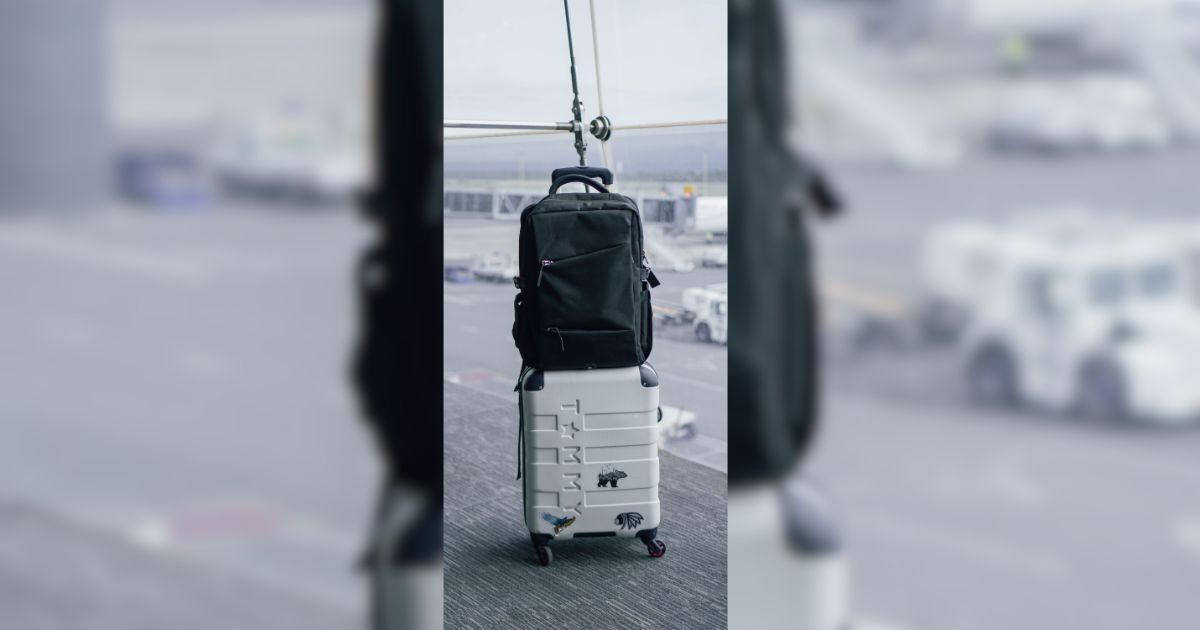 White carry-on suitcase with black backpack in an airport terminal
